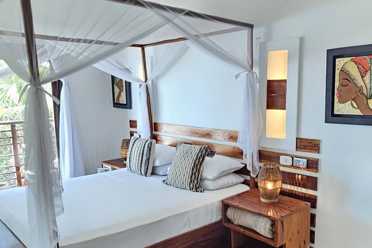 A four-poster bed with a canopy, a bedside table with a lamp, and a wall-mounted light fixture.