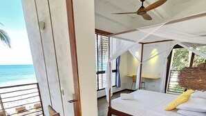 Un dormitorio con cama, ventilador de techo, mesita de noche y vista al océano.