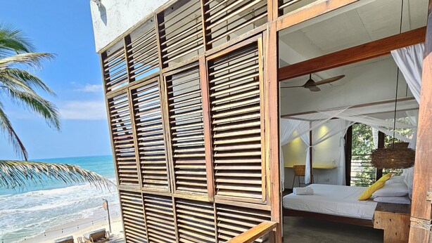 Una terraza de madera con una cama y vista a la playa.