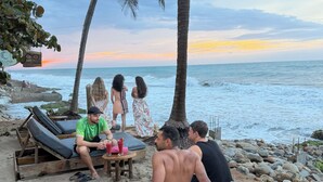 Um cenário à beira-mar com cadeiras de descanso, uma mesa com bebidas e vista para o oceano.