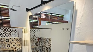Un baño con inodoro y lavamanos blancos, ducha, pared con diseño, espejo y un pequeño estante con una toalla.