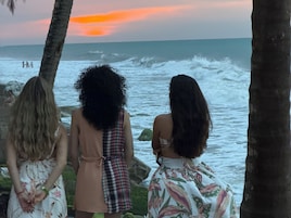 Tres personas de pie junto al océano, mirando el mar con olas.