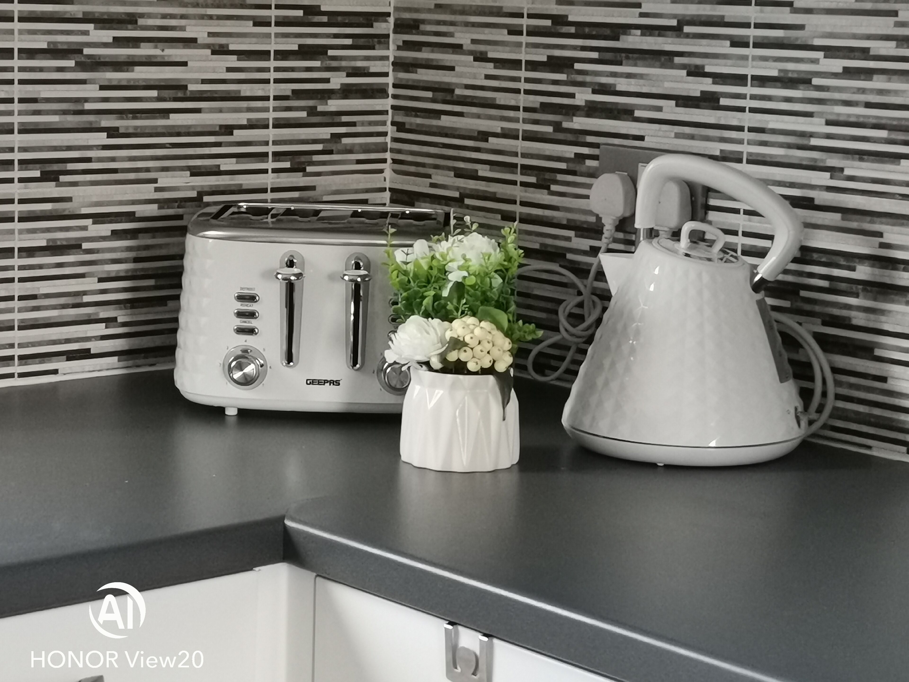 Una encimera de cocina con un tostador GEOPAS, un hervidor blanco y un florero con flores blancas.