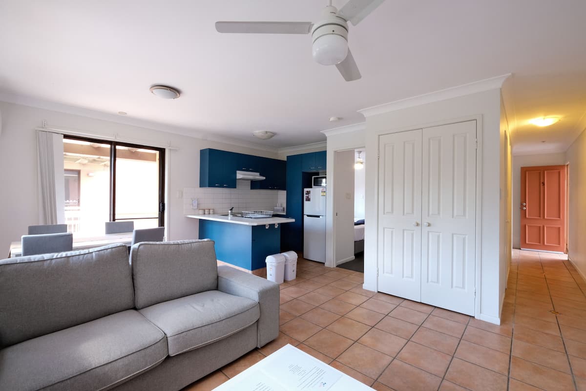 A living room with a sofa, a dining area with chairs, a kitchen with blue cabinets, and a white door.