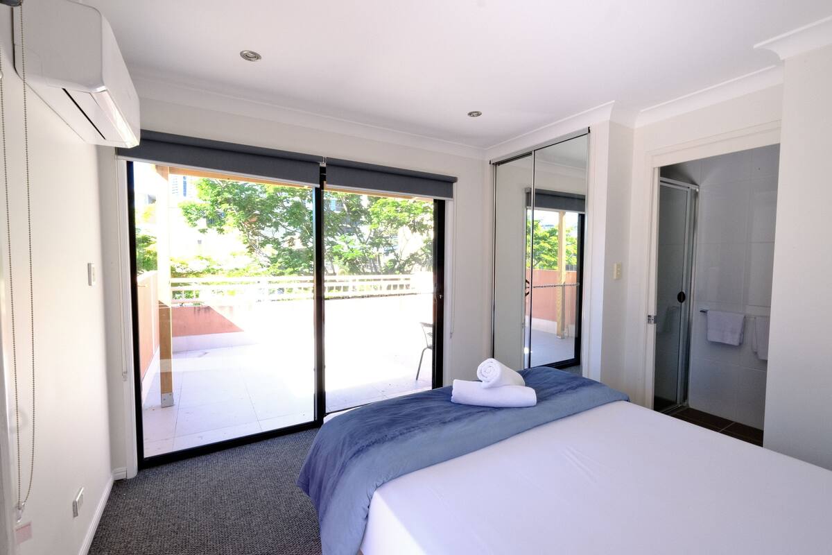 A hotel room with a large bed, a sliding glass door to a balcony, a shower, and a wardrobe.