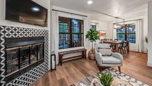 A modern living room with a fireplace, a dining area, and large windows with a view.
