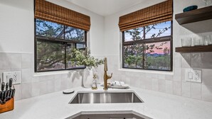 A kitchen with a stainless steel sink, two windows with bamboo blinds, and a countertop with a knife block.