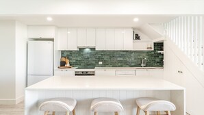 A modern kitchen with white cabinetry, a green backsplash, and a large island with bar stools. - THE Palms Angourie - Treetop Retreat Near Spooky Beach - Holiday Yamba (Angourie)