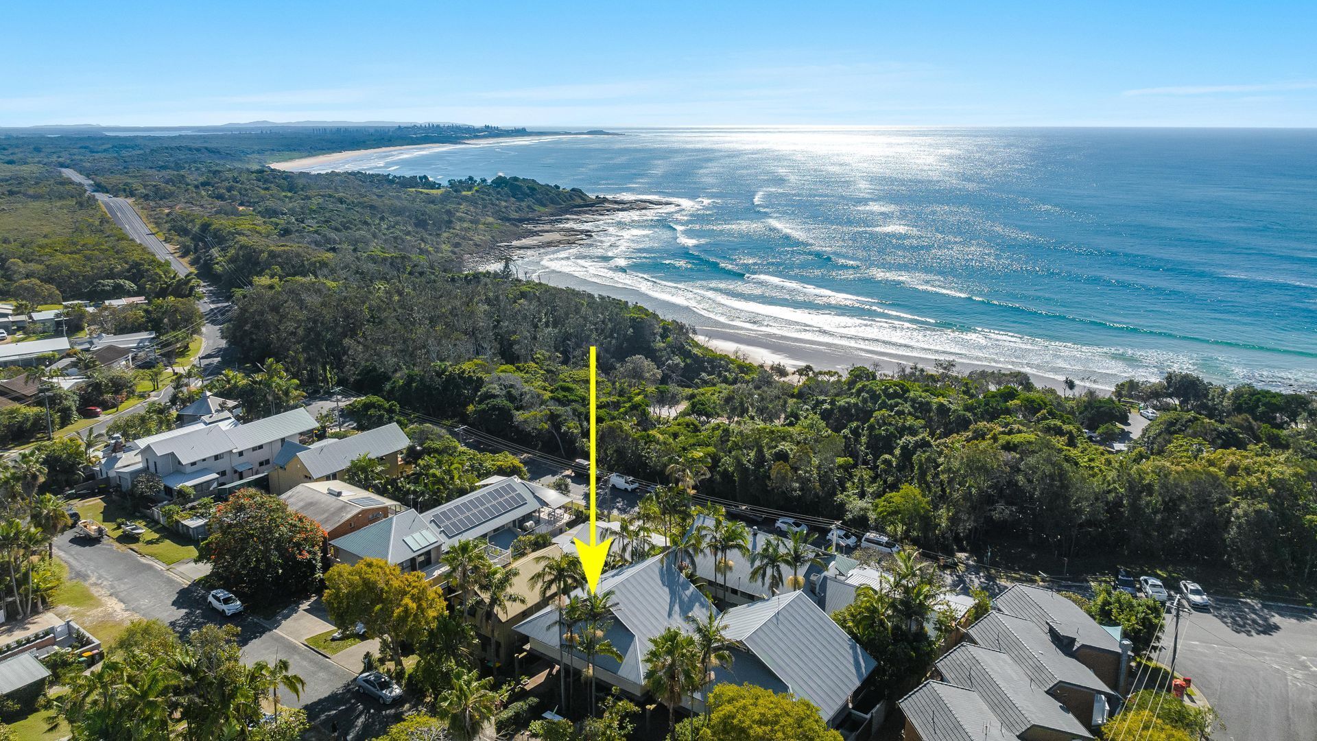 An aerial view of a coastal residential area with houses, a road, and a beach.