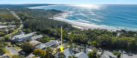 An aerial view of a coastal residential area with houses, a road, and a beach.