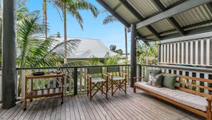 A wooden deck with a bench and chairs, surrounded by lush greenery and a building with a metal roof. - THE Palms Angourie - Treetop Retreat Near Spooky Beach - Holiday Yamba (Angourie)