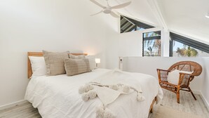 A bedroom with a bed, a ceiling fan, a window, and a wicker chair. - THE Palms Angourie - Treetop Retreat Near Spooky Beach - Holiday Yamba (Angourie)