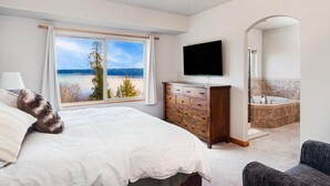Ein Schlafzimmer mit einem Bett, einer Holzkommode, einem Fernseher und Seeblick.