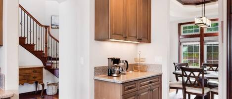 A kitchen with wooden cabinets, a coffee maker, and a dining area with chairs and a table.
