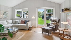 Een ruime woonkamer met een hoge plafond, een grote schuifpui naar een tuin, een witte bank, een ronde salontafel en een grijze fauteuil.