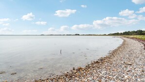 Een kiezelstrand met helder water en een verre kustlijn.