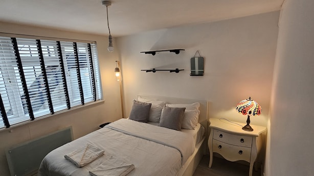 A bedroom with a bed, bedside table, lamp, and wall-mounted shelves. - Peaceful & Elegant (London)