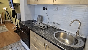 A compact kitchen with wooden cabinets, a stainless steel sink, and a tiled backsplash. - Peaceful & Elegant (London)