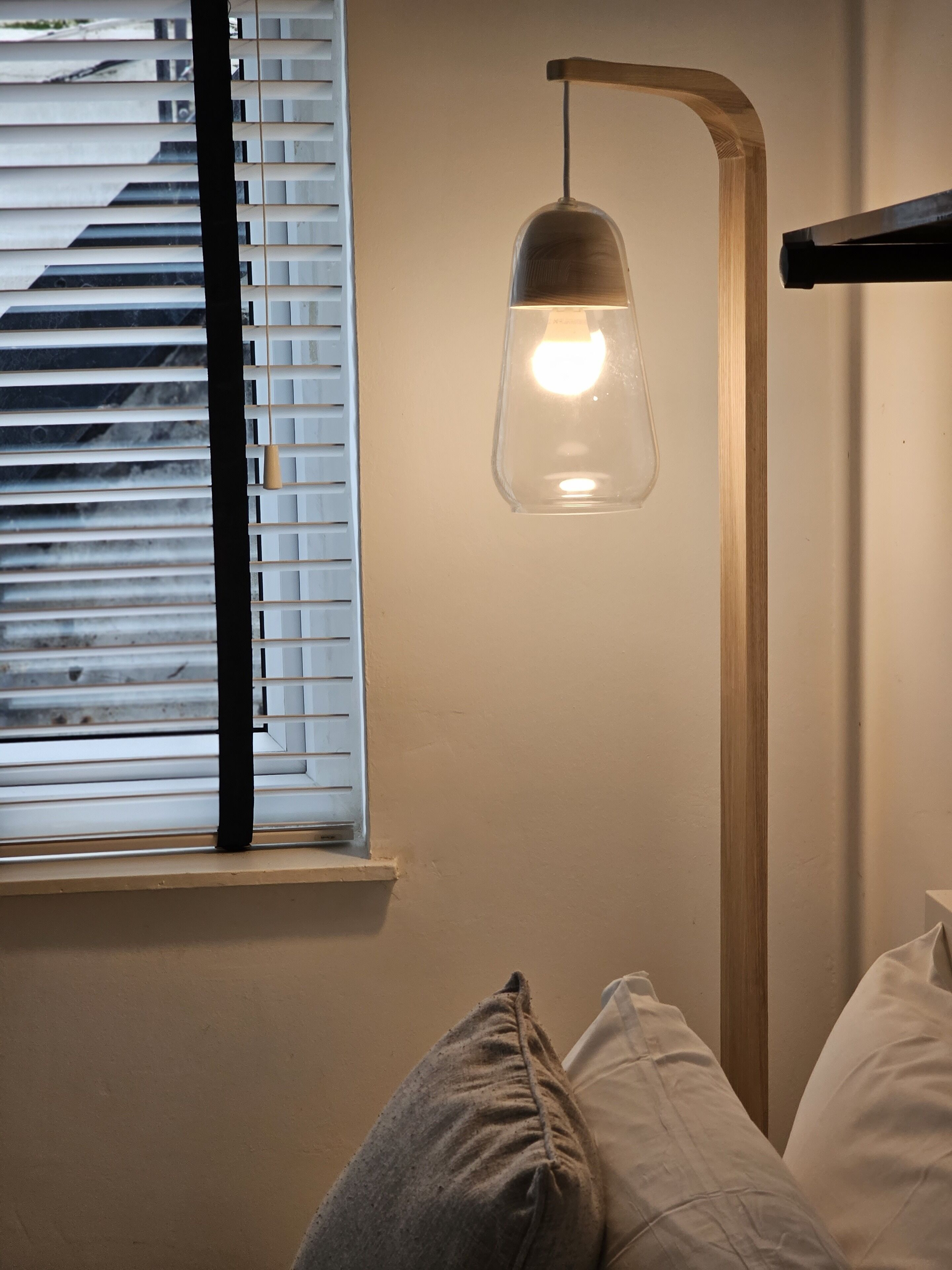 A room with a bed, a window with blinds, and a hanging pendant light.