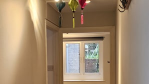 A hallway with a door leading to a room with a window, a blue chair, and a ceiling light fixture. - Peaceful & Elegant (London)