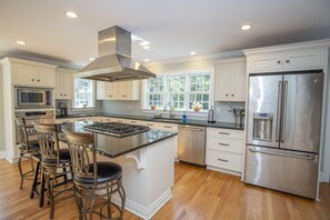 Una cocina moderna con armarios blancos, electrodomésticos de acero inoxidable y una isla central con taburetes de bar.