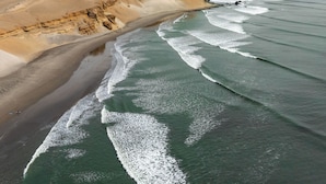 An aerial view of a coastal landscape with a sandy beach, waves, and distant mountains. - Hotel Sueños de Chicama (Rázuri)