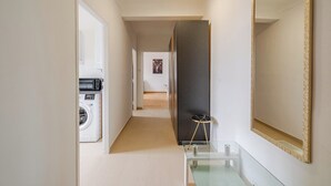 Un couloir avec un lave-linge, une table en verre et un grand miroir.