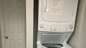 Un appareil combiné lave-linge et sèche-linge à chargement frontal, avec un panneau indiquant la présence d’un enfant asthmatique et interdisant de fumer.