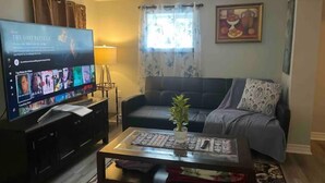 Un salon avec un téléviseur, un canapé, une table basse et une plante.