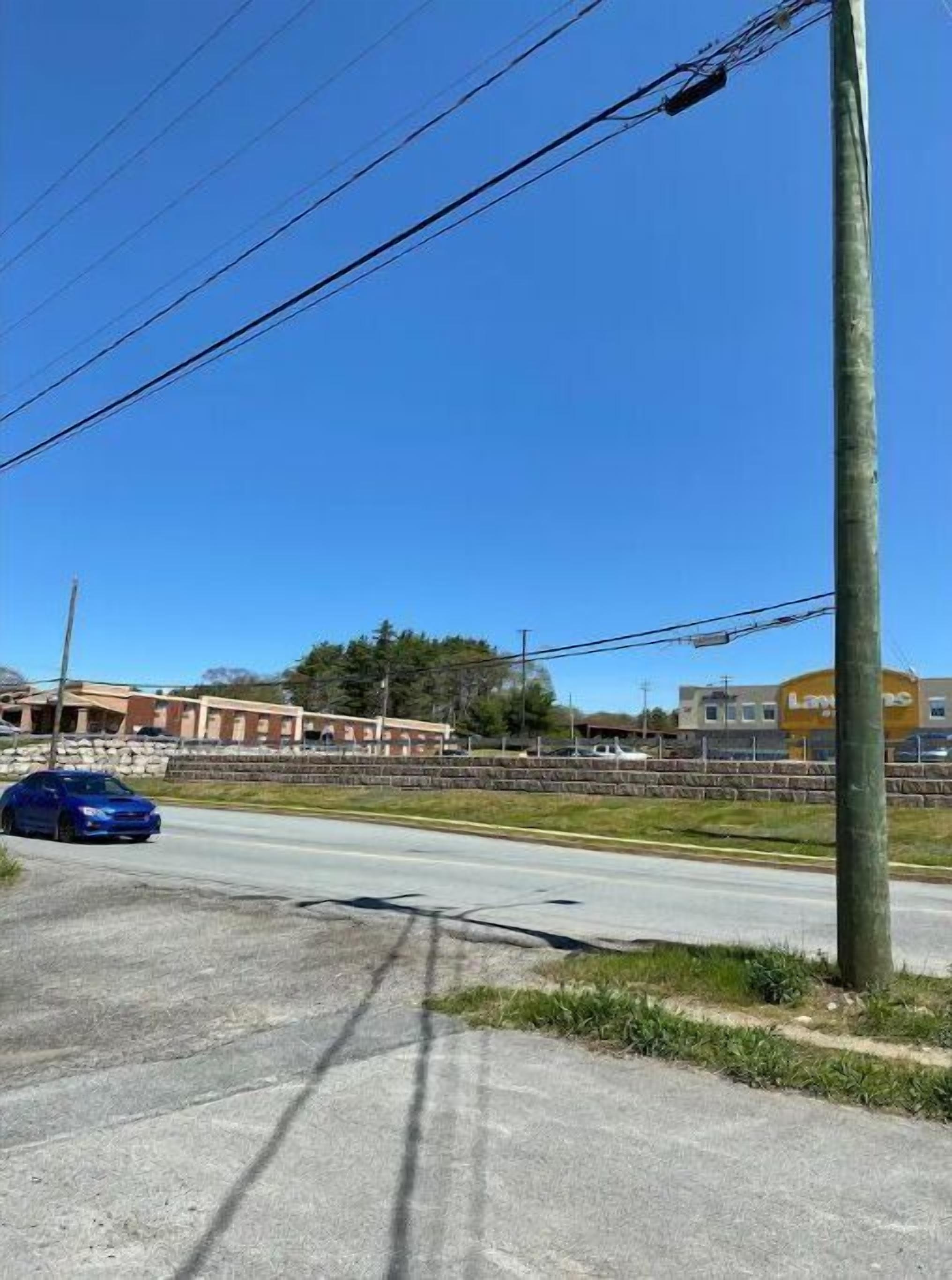 A road with a blue car, utility poles, and buildings in the background.