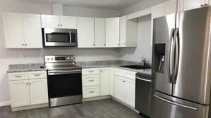 A modern kitchen with white cabinets, stainless steel appliances, and a grey floor. - Abigael’s Apt Suite 1 BR 2 BED in Central Bridgewater

 (Bridgewater)