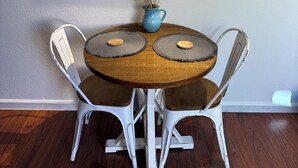 Une table à manger agrémentée d’un vase bleu et de fleurs séchées, entourée de chaises blanches à assise en bois, le tout placé devant un mur orné d’un tableau encadré.
