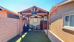 Un patio abrité avec une pergola en bois, un mur en briques et une fenêtre sur la droite.