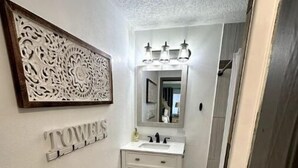 Un couloir étroit avec une coiffeuse blanche, un miroir et un élément décoratif mural.