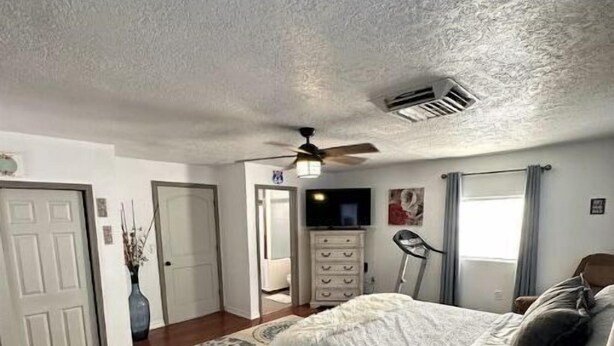 Une chambre à coucher comprenant un lit, un ventilateur de plafond, une commode, un téléviseur et une fenêtre avec des rideaux.