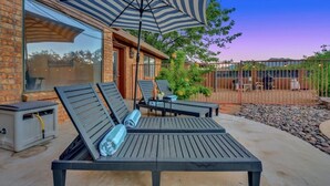 A patio with two lounge chairs, a striped umbrella, and a brick building. - NEW Mountain View 4 BDRM Home with Pool & Spa, right on a Golf Course (Sierra Vista)