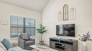 Una sala de estar con un sofá gris, una mesa de centro, un televisor sobre un mueble bajo y una planta.
