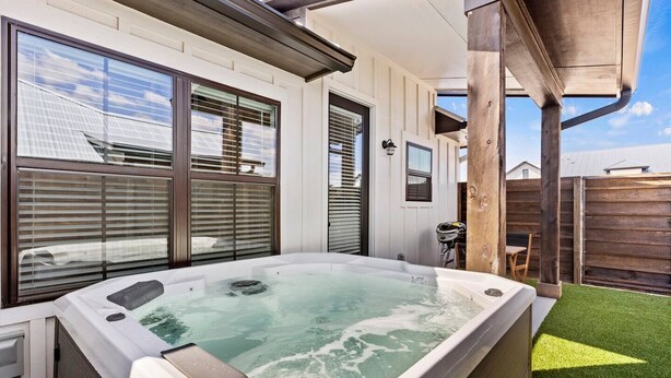 Un jacuzzi en un patio trasero con terraza de madera y valla blanca.