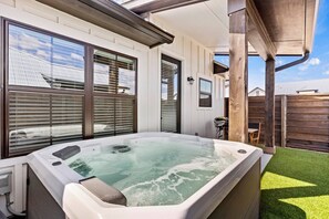 Un bain à remous dans un jardin, avec une terrasse en bois et une clôture blanche.