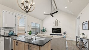 Una cocina amplia con una isla central, un comedor con sofá, y una sala de estar con televisor.