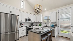 Una cocina moderna con electrodomésticos de acero inoxidable, una isla central con taburetes y una lámpara colgante.