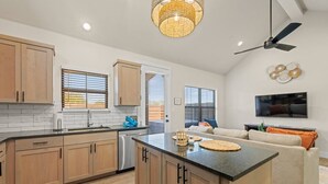 A modern kitchen with wooden cabinets, a central island, and a dining area with a sofa and TV. - *New Romantic Getaway|Hot Tub (Fredericksburg)