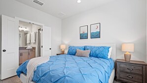 A bedroom with a large bed, a nightstand, a dresser, a door leading to a bathroom, and two wall-mounted pictures. - *New Romantic Getaway|Hot Tub (Fredericksburg)