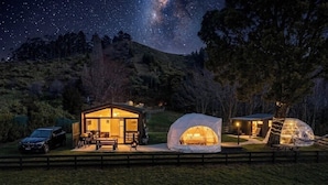 Un alojamiento acogedor al aire libre con una cabaña de madera y dos tiendas tipo cúpula, frente a un cielo estrellado.
