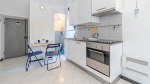 Cocina compacta con armarios blancos, horno de acero inoxidable y una pequeña zona de comedor con sillas azules.