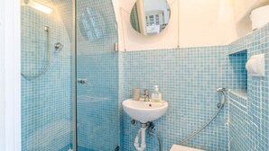 Un baño con paredes de azulejos azules, cabina de ducha de vidrio, lavamanos con espejo y un inodoro.