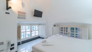 Habitación de hotel con cama, televisor montado en la pared, ventana con persianas y puerta que da a un balcón.