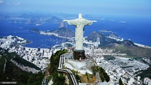 A statue with outstretched arms overlooking a coastal cityscape with mountains in the background.