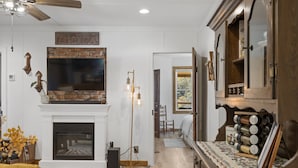 A living room with a fireplace, a television mounted above it, and a dining area with a table and chairs.