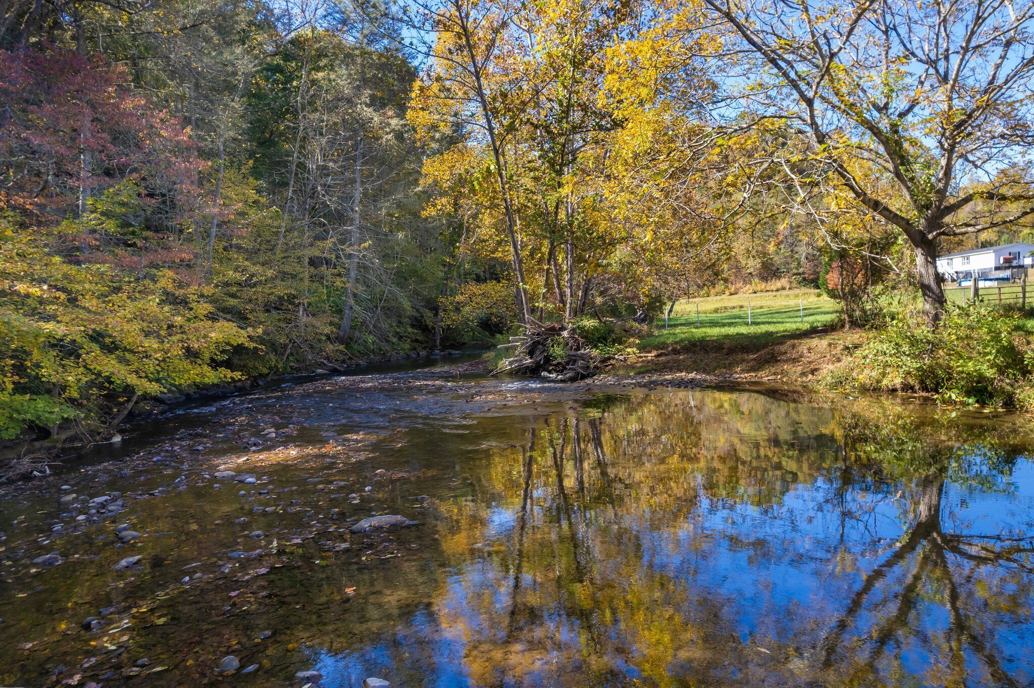 A river with clear water reflecting trees and a house in the background.
